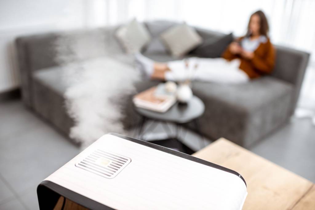 Active humidifier releasing mist while a woman relaxes on a couch behind it