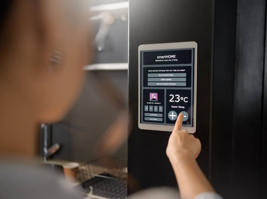 Smart IoT wall thermostat displaying heating controls as a woman monitors indoor temperature through a tablet