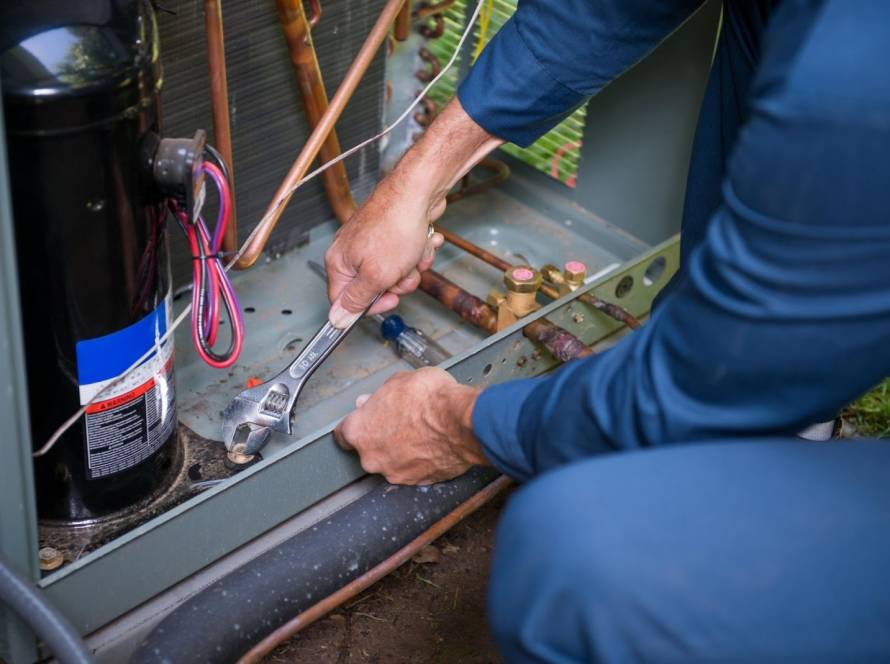Technician performing HVAC system repair on an outdoor unit using a wrench